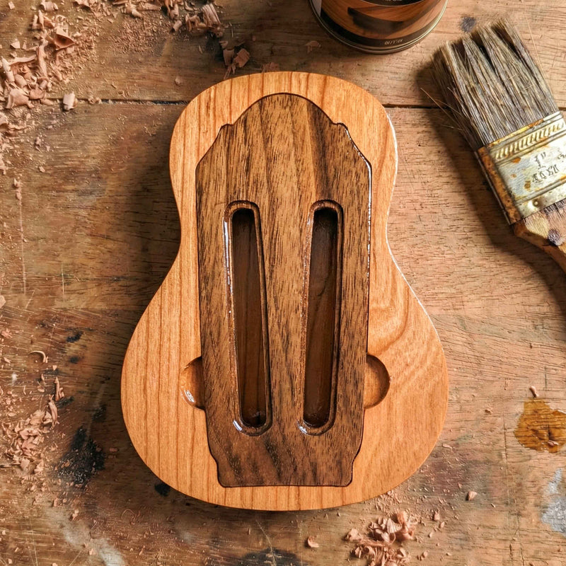 Wooden guitar pick case designed like a classical guitar slotted headstock, featuring two vertical slots and light wood grain finish.