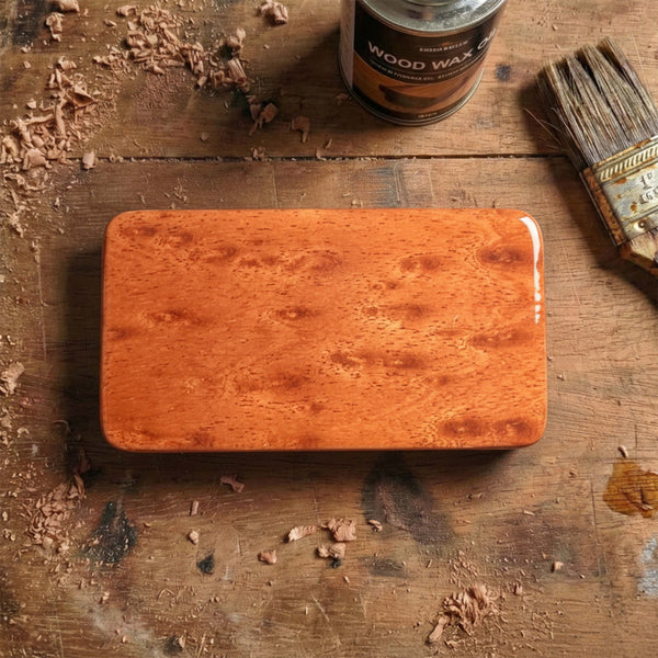 Rectangular wooden pick box featuring exotic burl wood grain with reddish tones, glossy finish, placed on a carpenter's workbench.