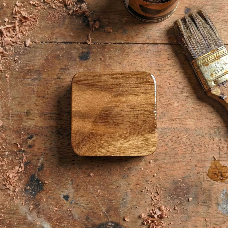 Smooth square walnut wood guitar pick holder with rounded corners and glossy finish, displaying natural wood grain on a workshop table.