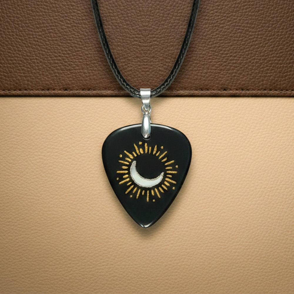 Black guitar pick pendant with a white crescent moon and gold sun rays design inlay.