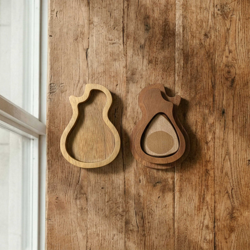 Organic guitar-body shaped wooden pick case with a pivoting cover. Features contrasting light and dark wood tones, open to reveal storage for a guitar pick.