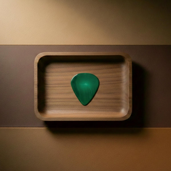 Deep green agate stone guitar pick with natural mineral aesthetics resting in a wooden display tray.
