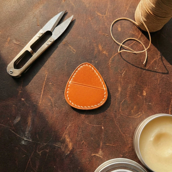 Minimalist orange-brown leather guitar pick case with hand-stitched detailing.