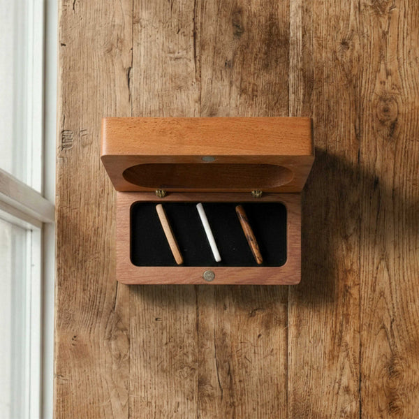 Rectangular wooden box designed for acoustic guitar bridge pins. Open hinged lid reveals a black foam insert holding three wooden string pegs.