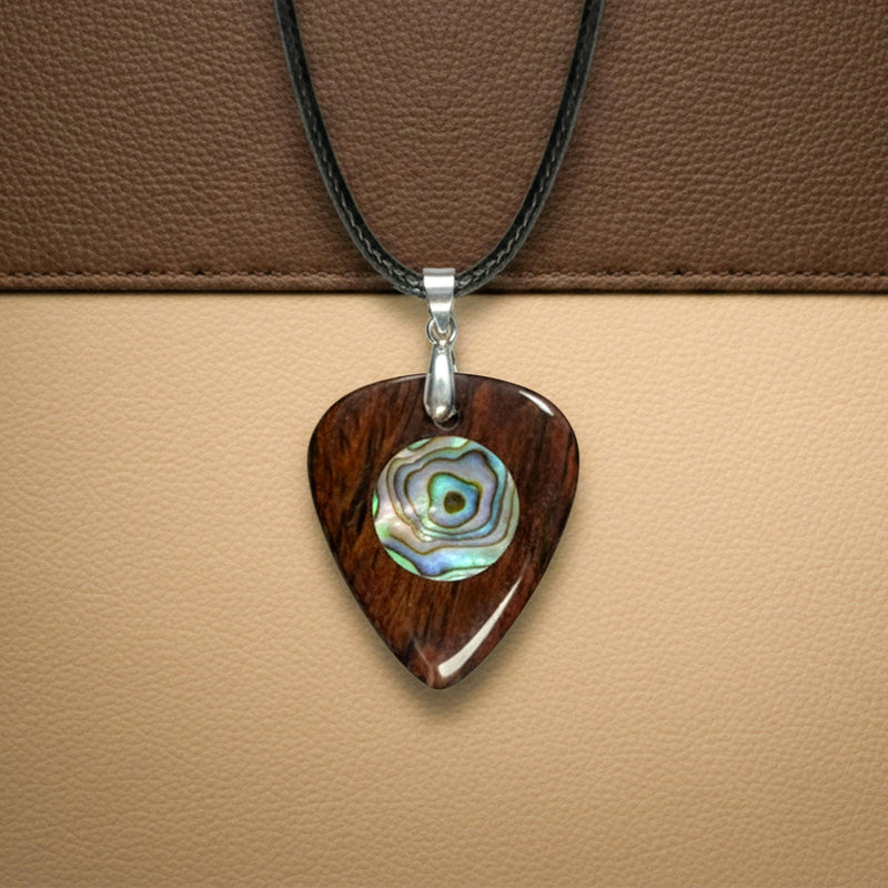 Dark wooden guitar pick pendant with a central circular abalone shell inlay. Handcrafted wood jewelry on a black leather cord.
