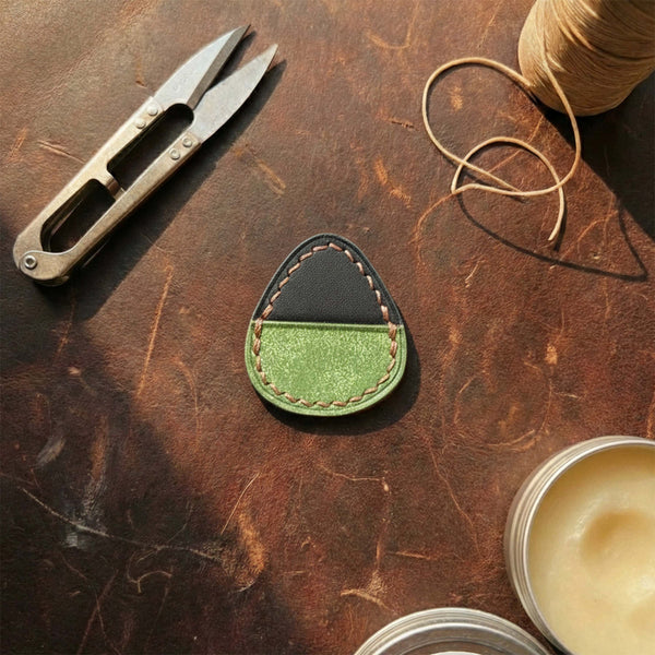 Hand-stitched leather guitar pick holder featuring black top and textured green bottom.