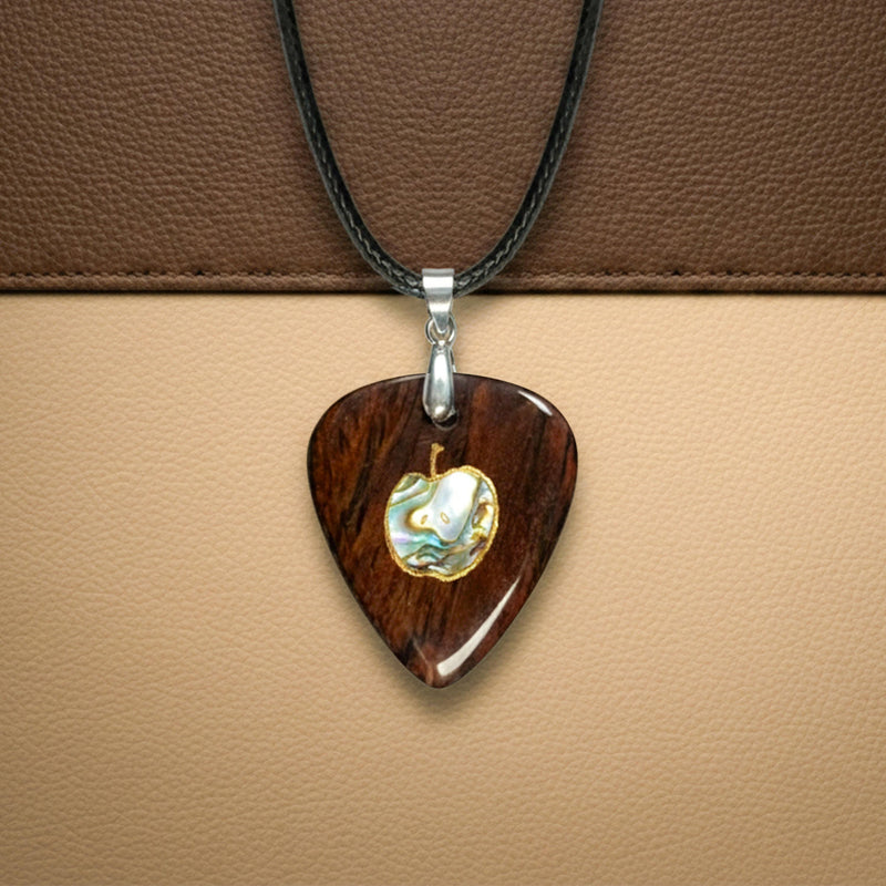 Dark wood guitar pick pendant with an apple-shaped abalone shell inlay outlined in gold. Minimalist fruit design jewelry for music lovers.