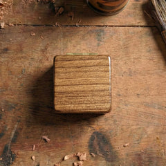 Square pick box made of walnut with visible brass hinges, closed lid showing horizontal wood grain texture.