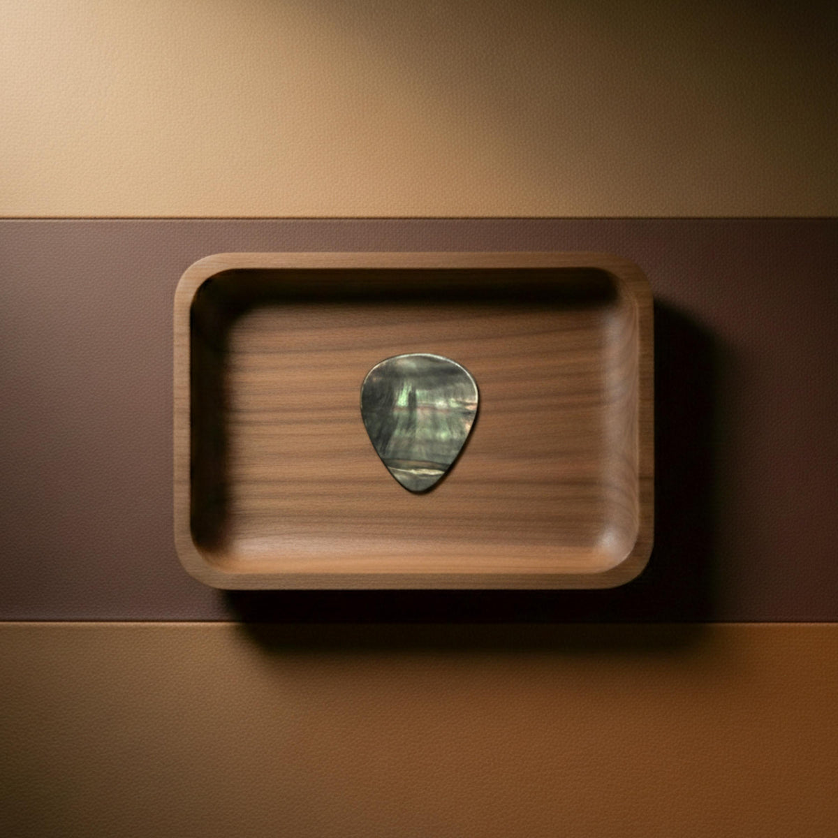 Handcrafted black mother of pearl guitar pick with iridescent shell texture displayed in a walnut wooden tray.