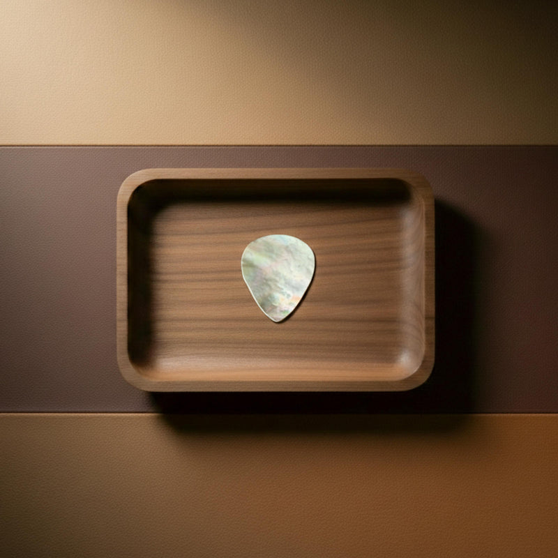 Gold and white mother of pearl guitar pick shimmering in a walnut wood tray, handcrafted plectrum.