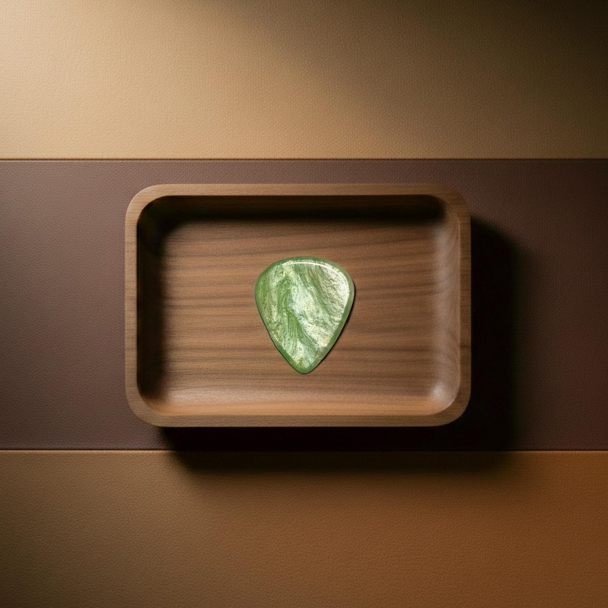 Green resin guitar pick featuring artistic white and metallic fluid patterns on a wooden surface.