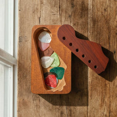 Rectangular wooden pick organizer with a swivel lid shaped like a guitar headstock. Shown open with multiple colorful picks inside for bulk storage.