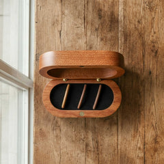Pill-shaped or oval wooden case for guitar bridge pins. Magnetic hinged lid opens to show a black foam insert with three slots for pins.