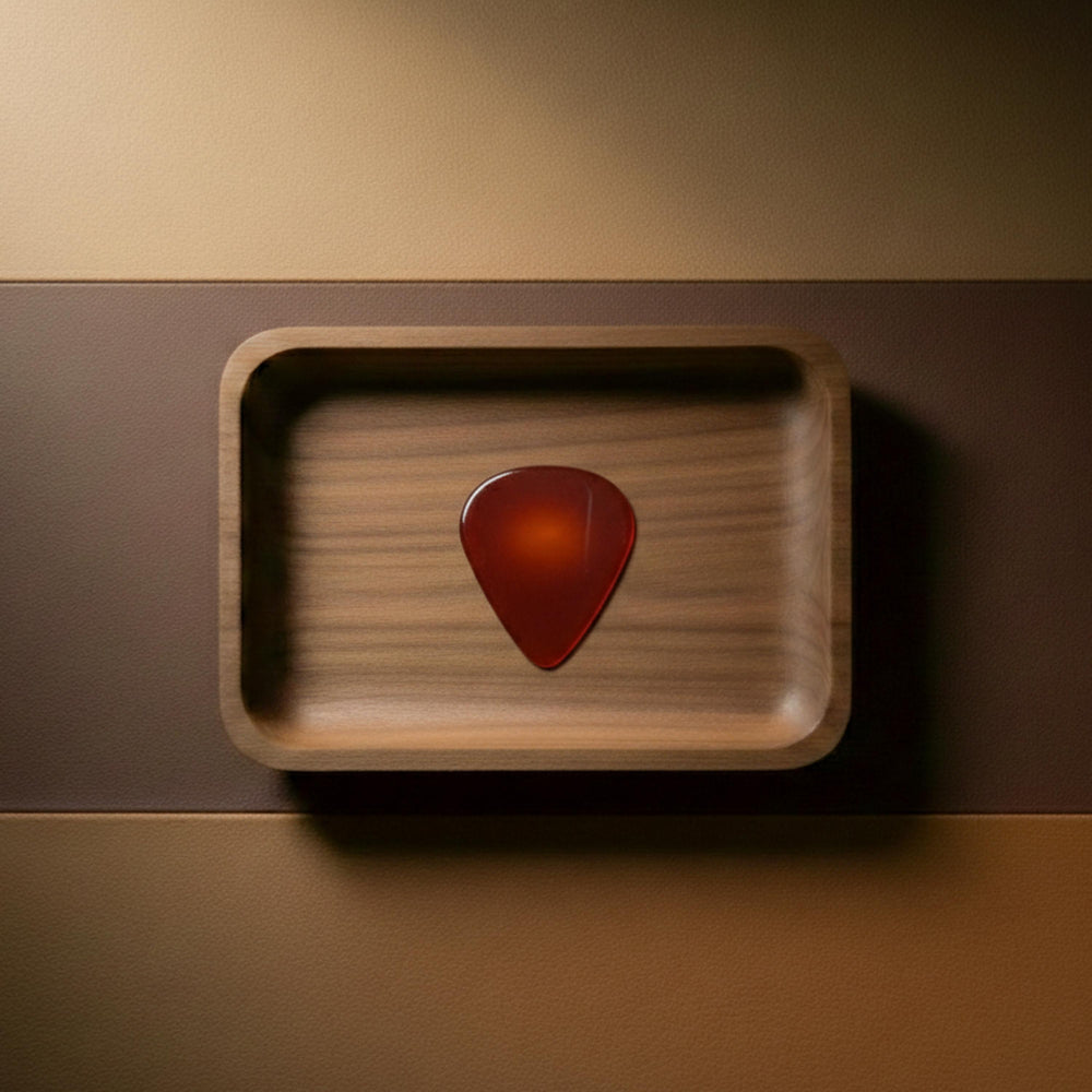 Translucent red agate guitar pick featuring warm orange and amber tones, set on a leather and wood background.