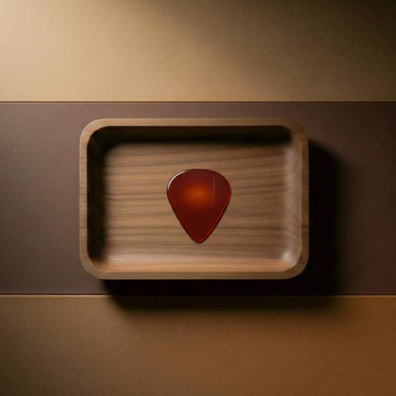 Translucent red agate guitar pick featuring warm orange and amber tones, set on a leather and wood background.