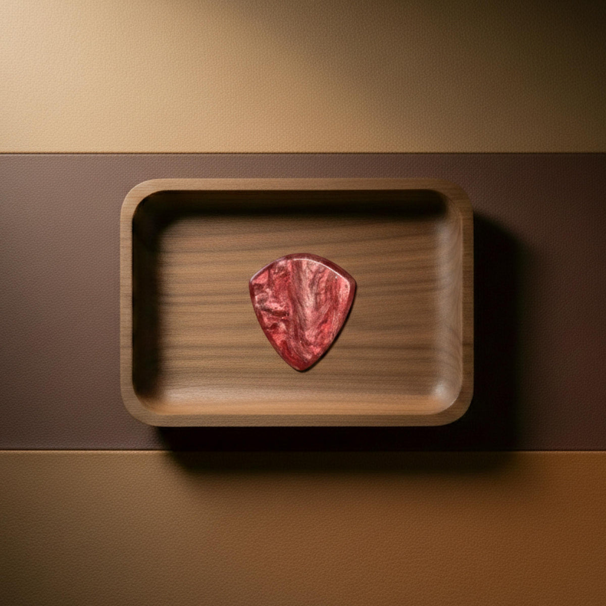 Red resin guitar pick with metallic shimmering swirls and unique patterns displayed in a wooden tray.